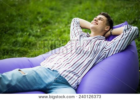 Handsome Young Man Lying On Inflatable Sofa Lamzac While Resting On Grass In Park