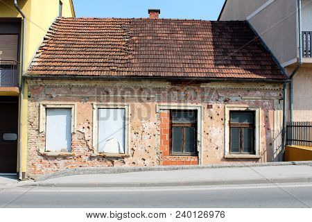 Small Attached House Damaged By Shrapnels During War With Falling Facade, Damaged Roof Tiles, Missin