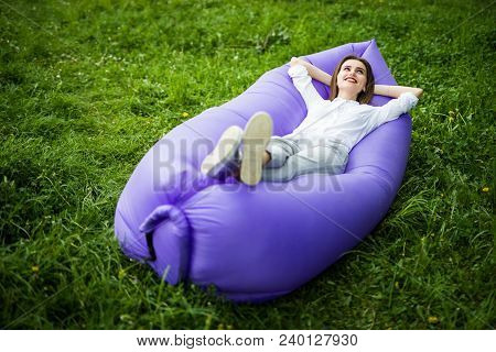 Pretty Young Woman Lying On Inflatable Sofa Lamzak While Resting On Grass In Park On The Sun