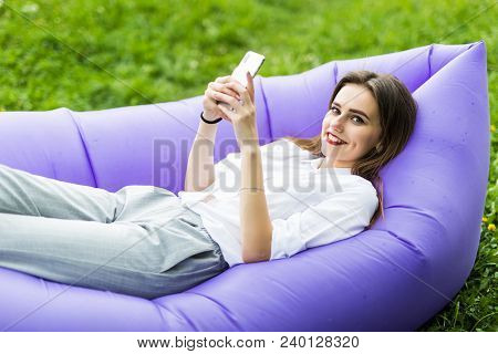 Pretty Young Woman Lying On Inflatable Sofa Lamzac Use App From The Phone, Browse Internet While Res