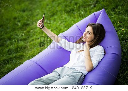 Relax On Fresh Air. Pretty Young Woman Lying On Inflatable Sofa Lamzac Use Mobile Phone While Restin