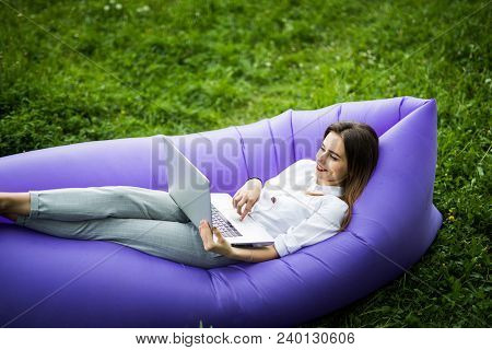 Pretty Young Woman Lying On Inflatable Sofa Lamzac Working On Laptop While Resting On Grass In Park