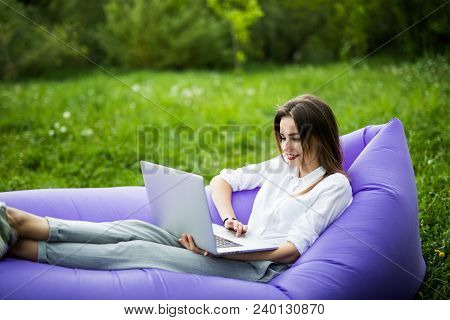 Pretty Young Woman Lying On Inflatable Sofa Lamzac Use Laptop While Resting On Grass In Park