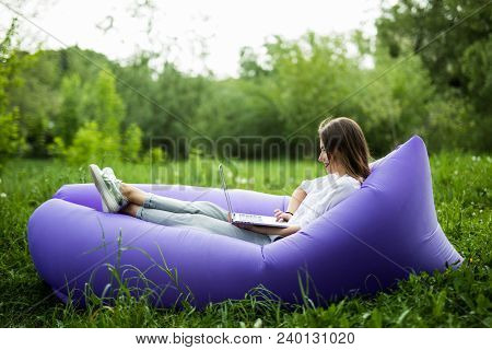 Pretty Young Woman Lying On Inflatable Sofa Lamzac Working On Laptop While Resting On Grass In Park