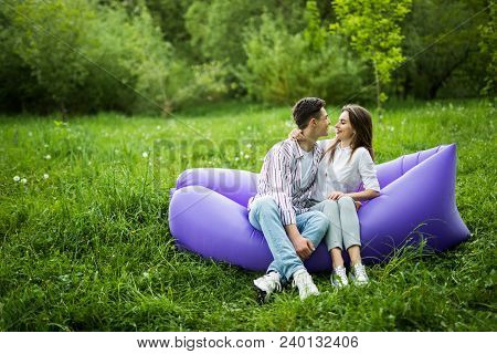 Love Couple Lying On Inflatable Sofa Lamzac On Laptop While Resting On Grass In Park Looking Each Ot