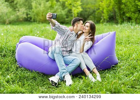 I Love You Too Much. Young Couple Kissing Sitting On Inflatable Sofa Lamzac And Take Selfie On Phone