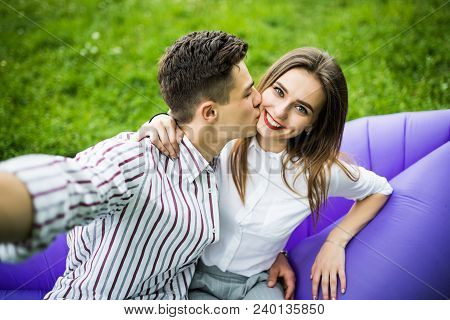 Young In Love Couple Kissing While Sitting On Inflatable Sofa Lamzac And Take Selfie On Phone Restin