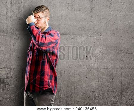 Young handsome man with sleepy expression, being overworked and tired, rubbes nose because of weariness