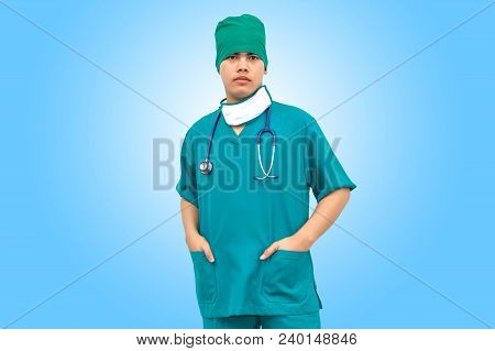 Asian Smart Doctor Wearing Green Uniform And Medical Face Mask With Stethoscope. Isolated On Blue Ba