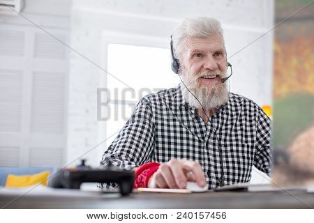 Avid Player. Upbeat Senior Man Sitting At The Table And Playing A Video Game Online With His Friends