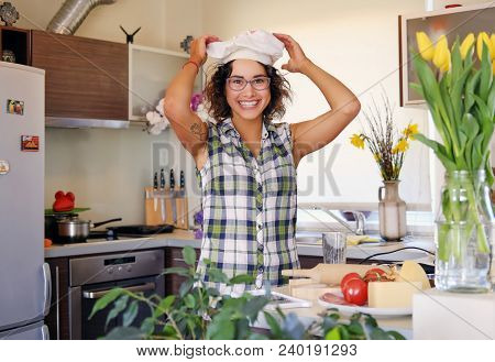 Portrait Of Brunette Attractive Female With Curly Hair In A Home Kitchen With A Lot Of Flowers.