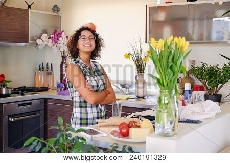 Portrait Of Brunette Attractive Female With Curly Hair In A Home Kitchen With A Lot Of Flowers.