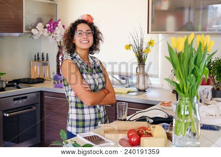 Portrait Of Brunette Attractive Female With Curly Hair In A Home Kitchen With A Lot Of Flowers.