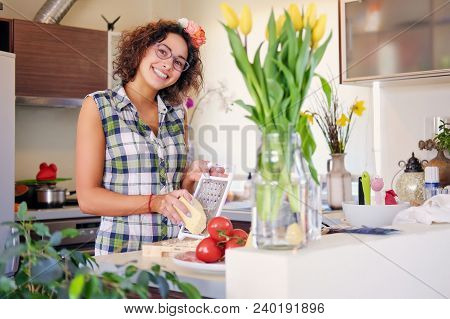 Positive Brunette Female With Curly Hair Makes Salad With Tomatoes And Potato In A Home Kitchen.
