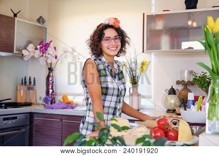 Portrait Of Brunette Attractive Female With Curly Hair In A Home Kitchen With A Lot Of Flowers.