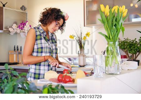 Attractive Brunette Female In Eyeglasses Making Salad From Vegetables In The Home Kitchen.
