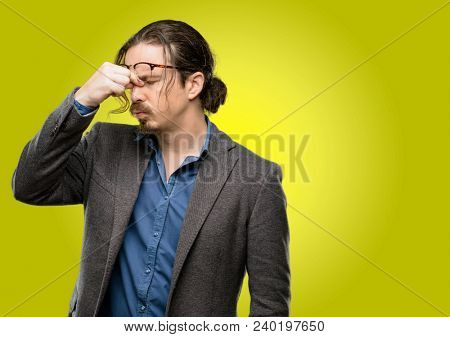 Handsome young man with sleepy expression, being overworked and tired, rubbes nose because of weariness