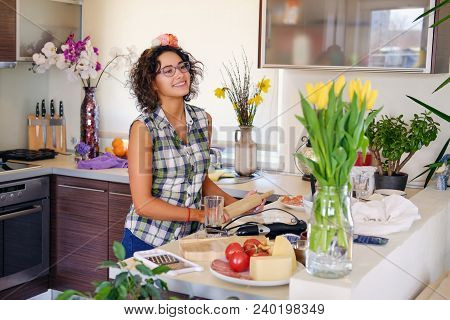 Portrait Of Brunette Attractive Female With Curly Hair In A Home Kitchen With A Lot Of Flowers.