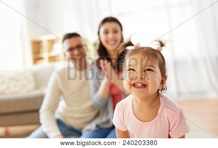family and people concept - happy little daughter with mother and father at home