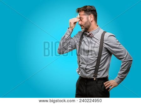 Middle age man, with beard and bow tie with sleepy expression, being overworked and tired, rubbes nose because of weariness
