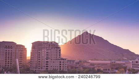 Sun setting over Scottsdale, Arizona waterfront area with Camelback Mountain glowing.