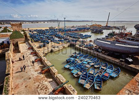 Essaouira Port In Morocco With Blue Fishing Boats And Ancient Famous Fort On Background On A Sunny D