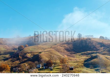 Autumn Carpathian Mountains Landscape With Trees And Small Hamlet On Slope, And Misty Cloud Over (ra