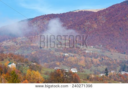 Autumn Carpathian Mountains Landscape With Multicolored Trees And Small Hamlet On Slope, And Misty C