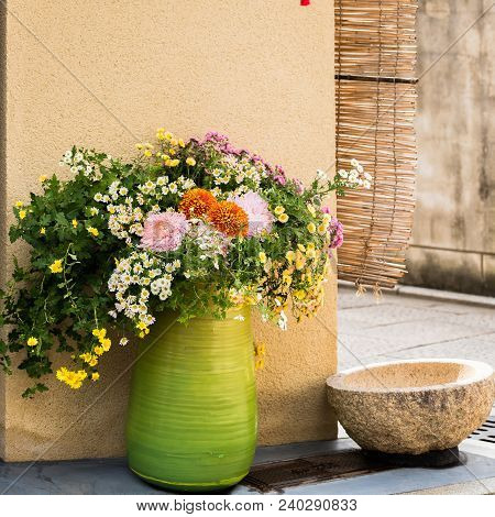 Green Vase With Wild Flowers On A City Street In Kyoto, Japan. Copy Space For Text.