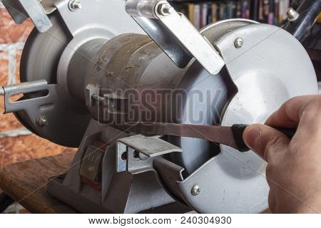 A Knife Sharpener And Hand With A Blade On A Wooden Table, Close-up Against A Brick Wall Background