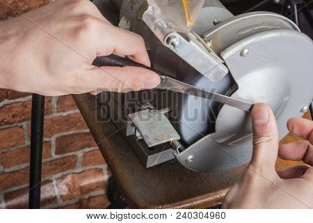 A Knife Sharpener And Hand With A Blade On A Wooden Table, Close-up Against A Brick Wall Background