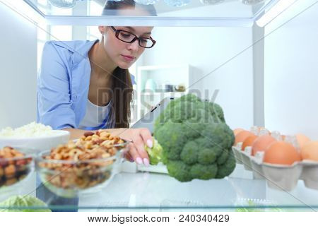 Portrait of female standing near open fridge full of healthy food, vegetables and fruits. Portrait of female