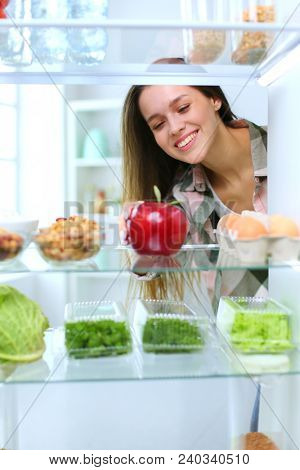 Portrait of female standing near open fridge full of healthy food, vegetables and fruits. Portrait of female