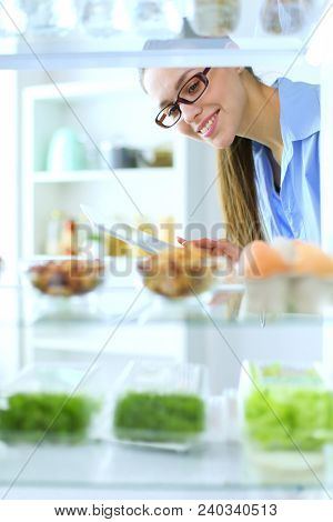 Portrait of female standing near open fridge full of healthy food, vegetables and fruits. Portrait of female