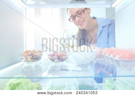 Portrait of female standing near open fridge full of healthy food, vegetables and fruits. Portrait of female