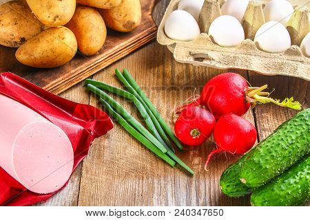 Ingredients For Okroshki - Sausage, Eggs, Radishes, Onions, Potatoes, Cucumbers On An Old Wooden Tab