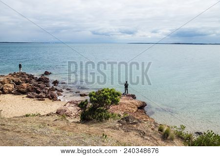 Two Fishermen On The Red Rocks At Erehwon Point Beach, Cowes, Phillip Island, Victoria, Australia