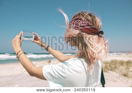 Young woman resting on the sand beach and taking photo with mobail phone