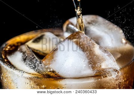 Stream Of Soda Being Pouring Into A Glass With Soda And Ice Cube On Black Background, Closeup Textur