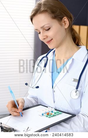 Woman Doctor Write Prescription While Sitting In Hospital Office. A Lot Of Various Colored Pills Liy