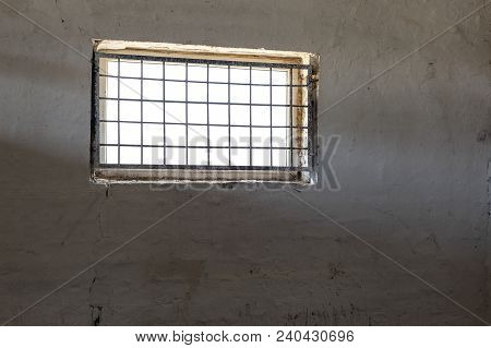 Old White Wall With Window Covered By Iron Grate. Sun Shining  Through Grill. Prison Room Interior .