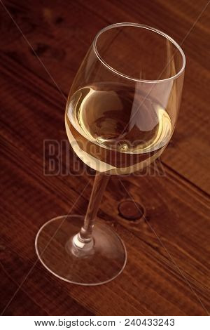 Closeup Photo Of One Full Clear Glass Goblet With White Semisweet Grape Wine Standing On Brown Woode