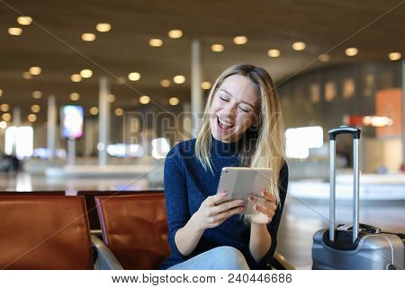 Caucasian Young Woman Sitting In Airport Waiting Room With Valise And Using Tablet. Concept Of Moder