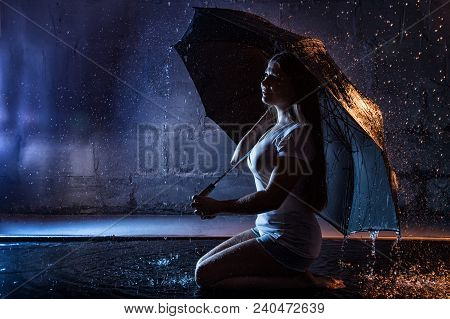Girl In The White Shirt With Black Umbrella, Water Drops Around And Dark Walls Background Illuminate