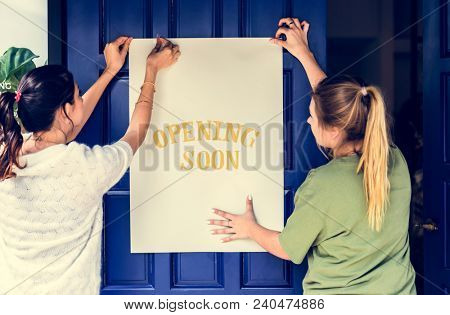 Women putting on store opening soon sign