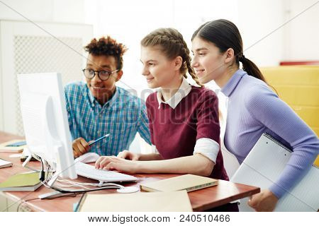 Three young start-upers looking at computer monitor while watching webcast after lessons