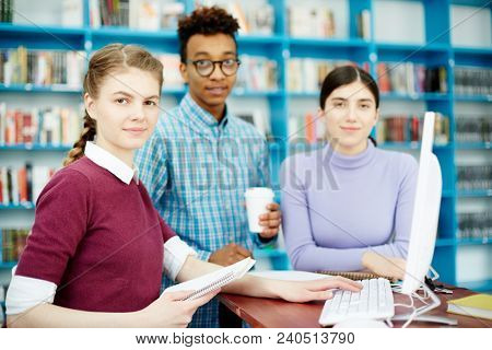 Young team of programmers carrying out group assignment in colleage library by computer
