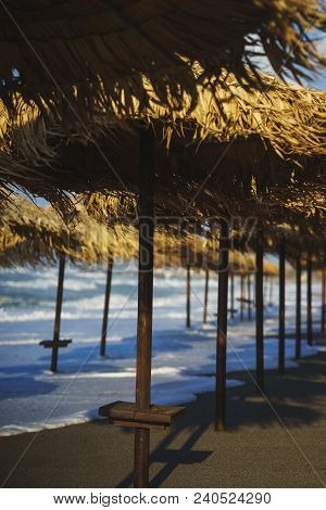 Vacation, Travel, Beach And Beach Umbrellas From The Straw During The Tide. Sea Waves And Empty Sand