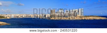 Malta, Valletta. Sliema town with multistorey waterfront buildings, blue sea and blue sky with few clouds background. Panoramic view, banner.