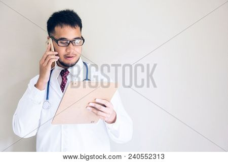 Handsome Asian Doctor At Emergency Room (er) Talking With Patient Relative By Smartphone While Readi